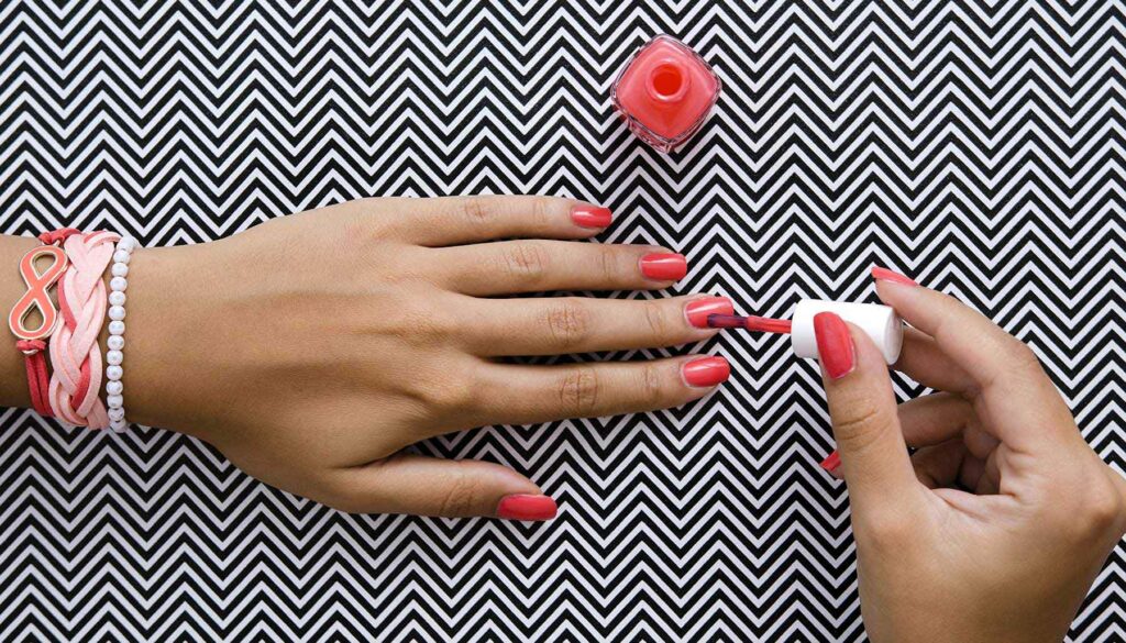 painting nails with coral nail polish against a black and white background