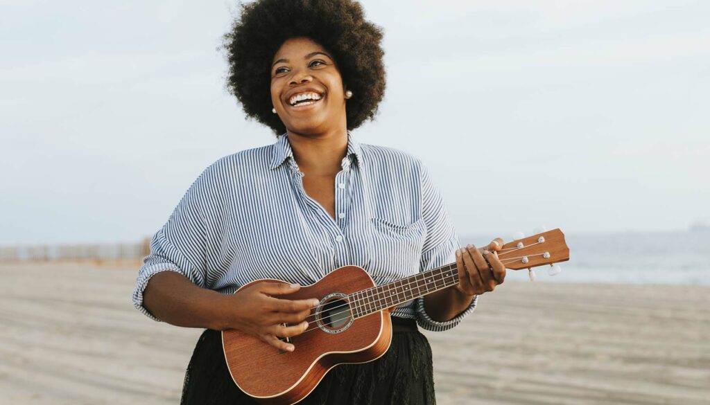 Happy woman playing a ukulele on the beach