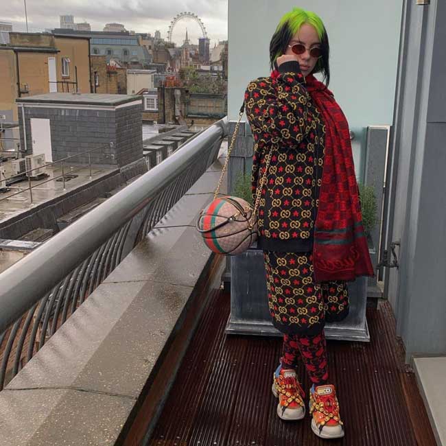 Billie Eilish wearing lots of patterns, ball shaped purse, and chunky sneakers