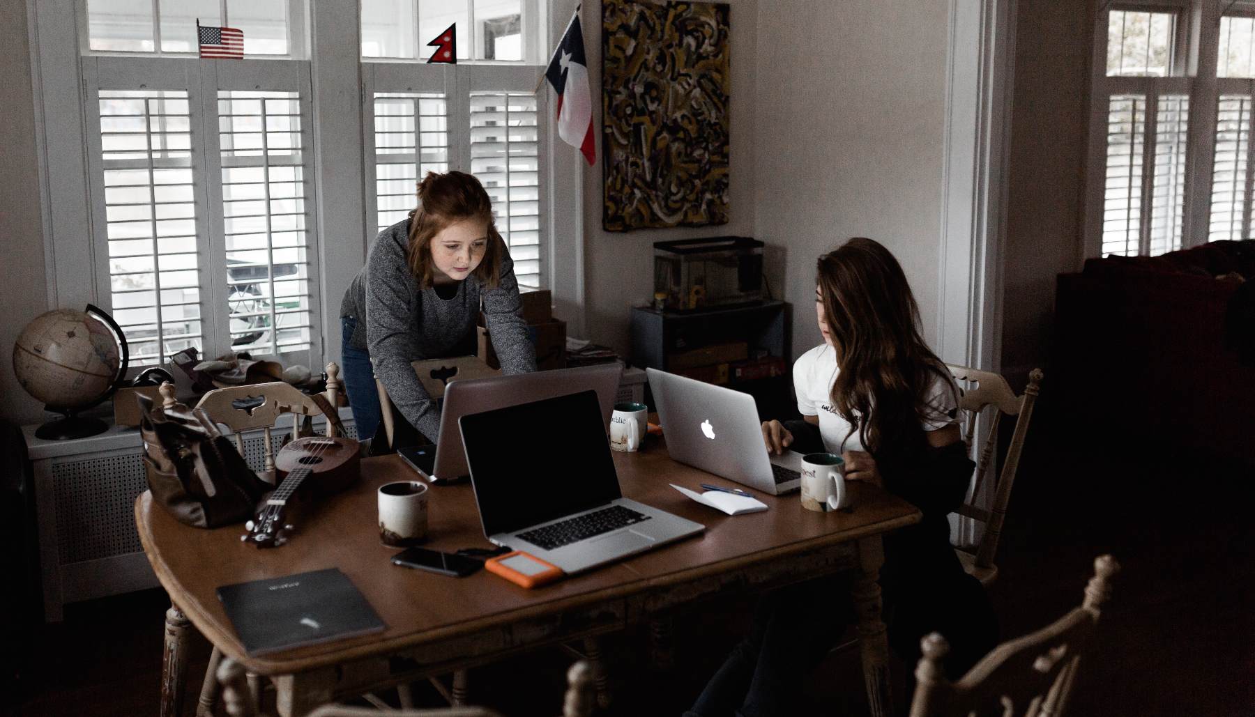 women working at a desk with many laptops