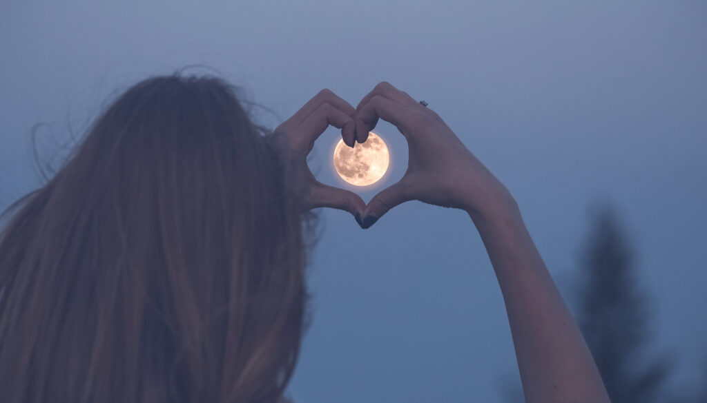 Woman forming a heart around the moon