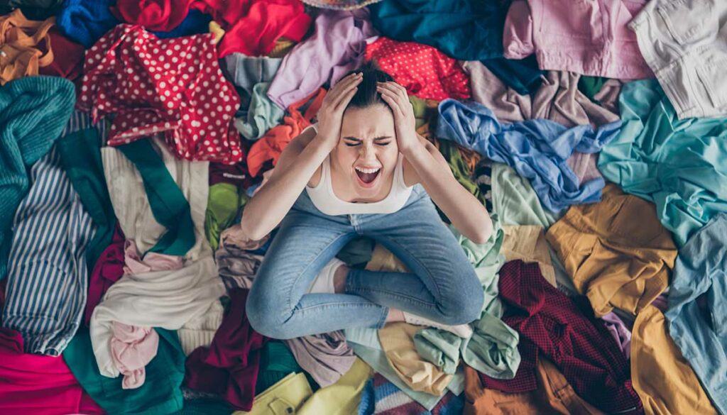 Help. High angle above view photo of stressed yelling lady stay home spring, cleaning household sit many clothes stack floor pick select look outfit nothing to wear hands on head indoors