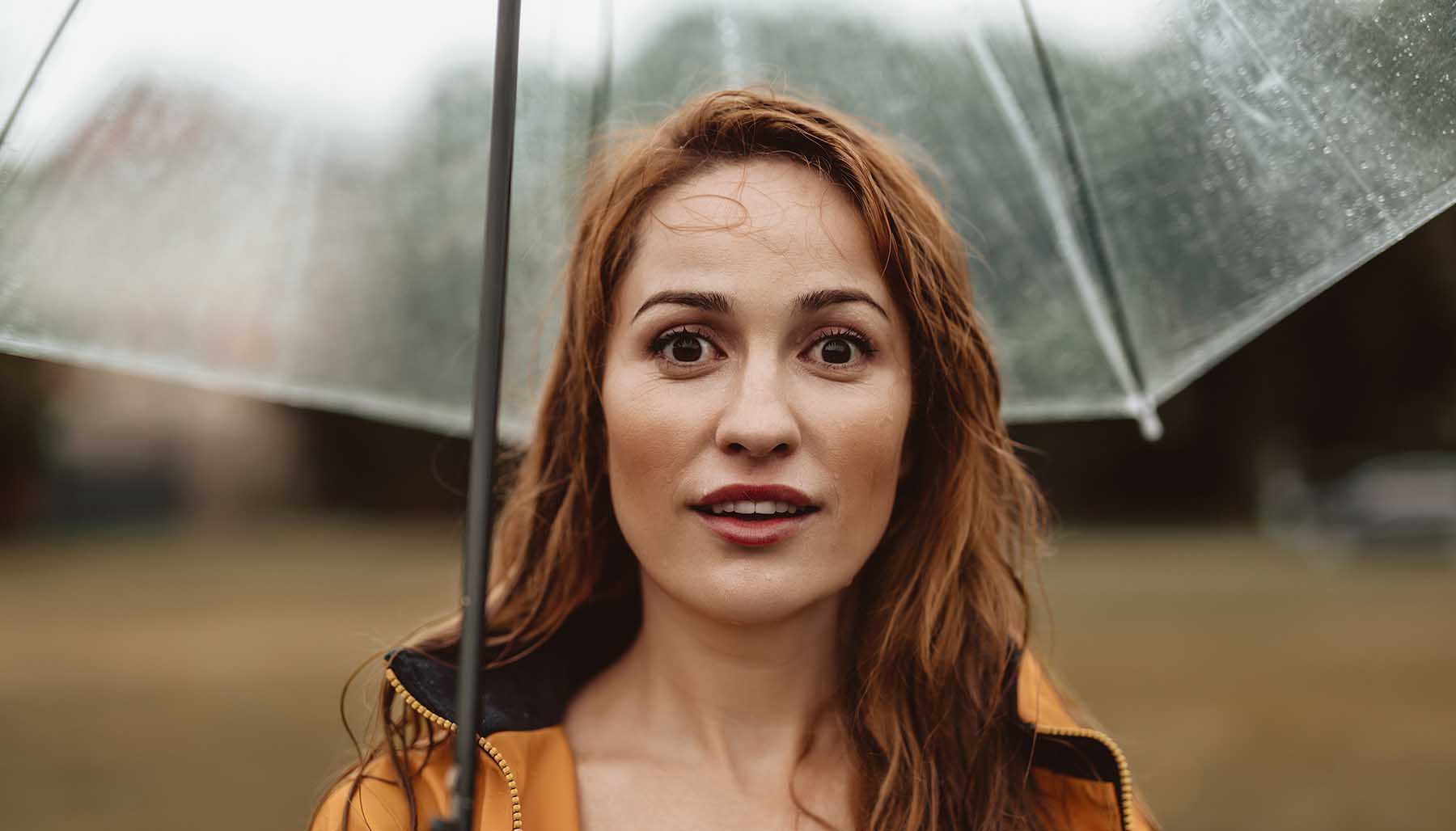 A redheaded woman standing in the rain under an umbrella