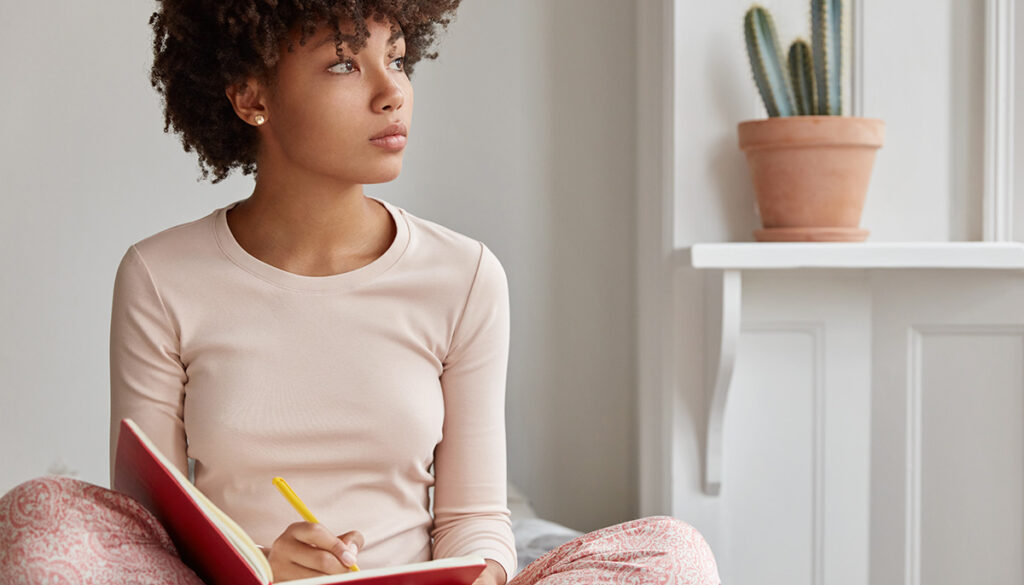 woman-sits-on-bed-to-write-in-journal