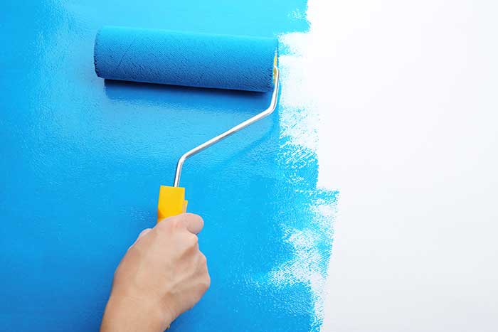 hand holding paint roller, painting the wall bright blue