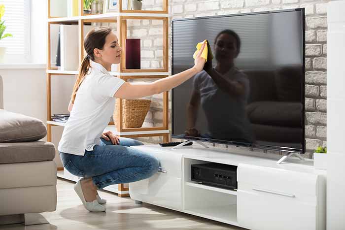 woman cleaning, wiping a flatscreen tv in the living area