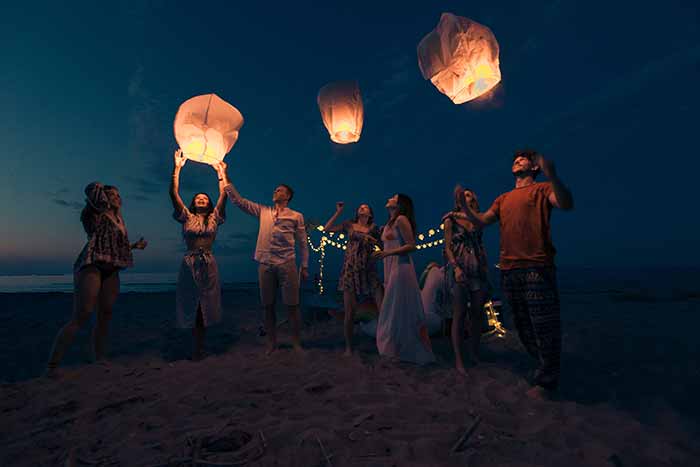 people launching sky lanterns at night on the beach