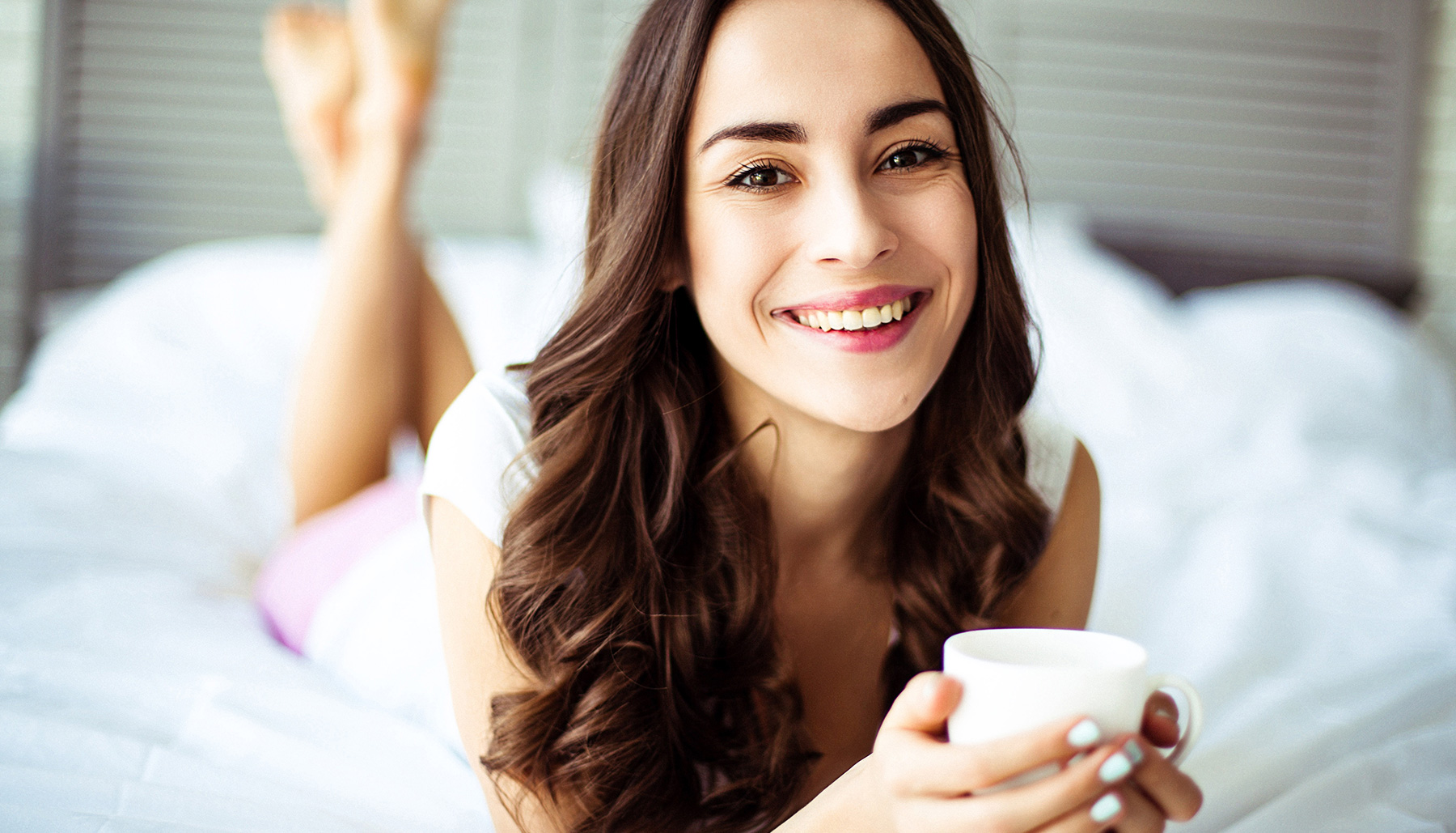 woman-holds-mug-and-lays-on-bed-smiling