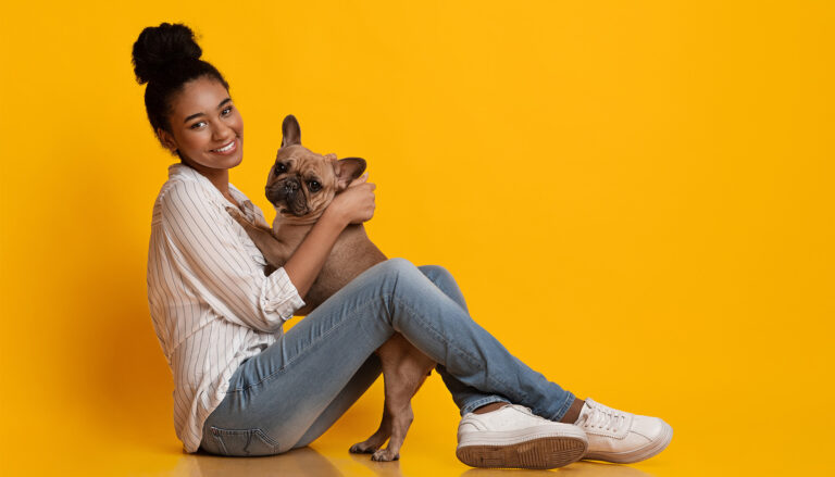 woman-smiles-with-dog-against-yellow-wall
