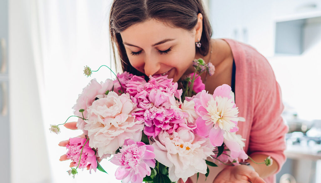 Happy woman smelling bouquet of peonies.