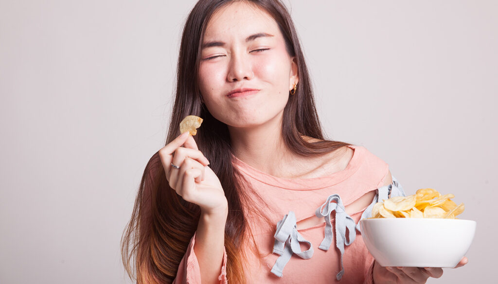 Woman closing eyes and eating potato chips