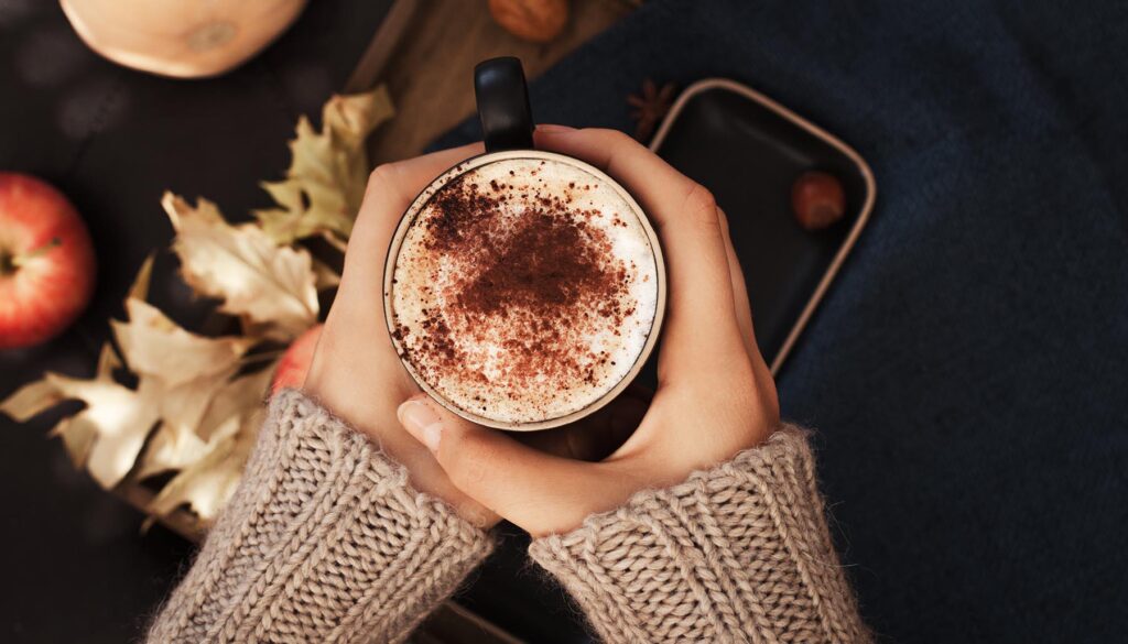 Female holding cup of pumpkin spice latte coffee, Autumn fall mood, holding hands, top view , warm and cozy. Copy space.