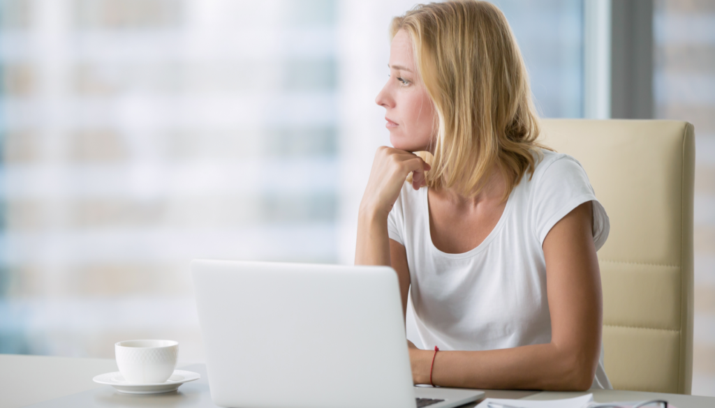 woman at desk with laptop staring out of window
