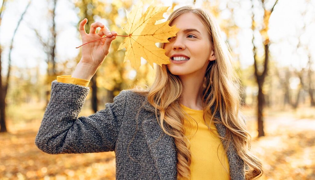 Portrait of a beautiful happy woman with a smile with autumn yellow leaf in the Park
