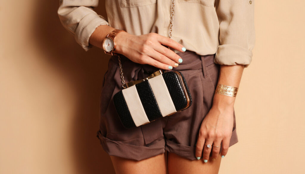 Girl wearing brown shorts and shirt with manicure, watch, and striped purse 