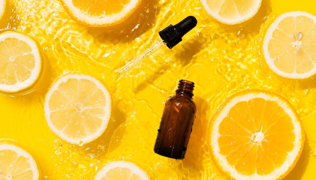 vitamin c serum in splashing water, surrounded by orange and lemon slices