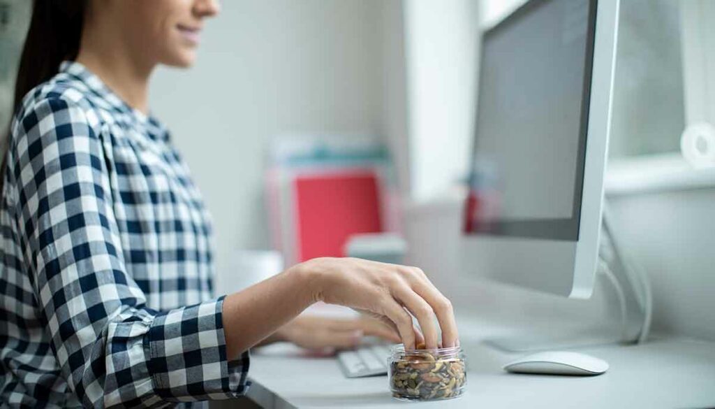 woman sitting at desk, snacking on nuts and seeds