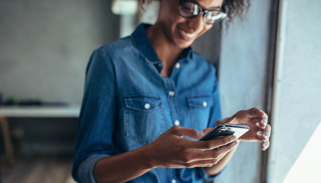 Female entrepreneur standing in office and using smart phone. Focus on mobile phone in hand of a woman wearing casuals.