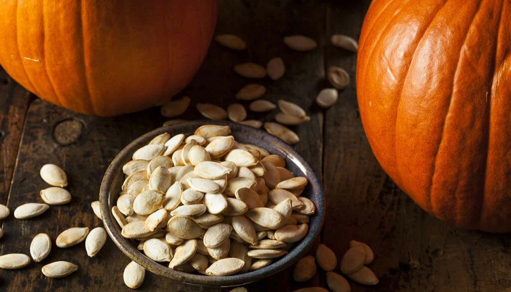 roasted pumpkin seeds in a bowl, in front of pumpkins
