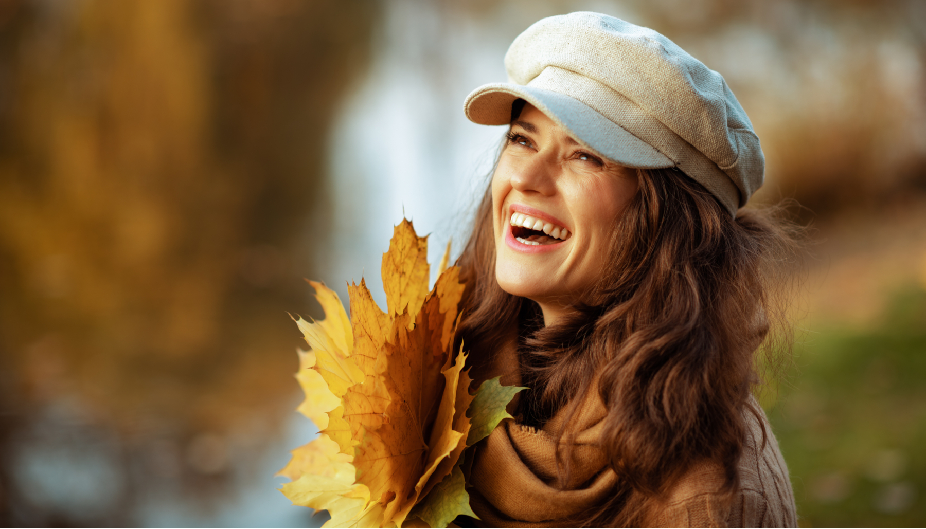 feature image woman with hat and scarf smiling holding fall leaves