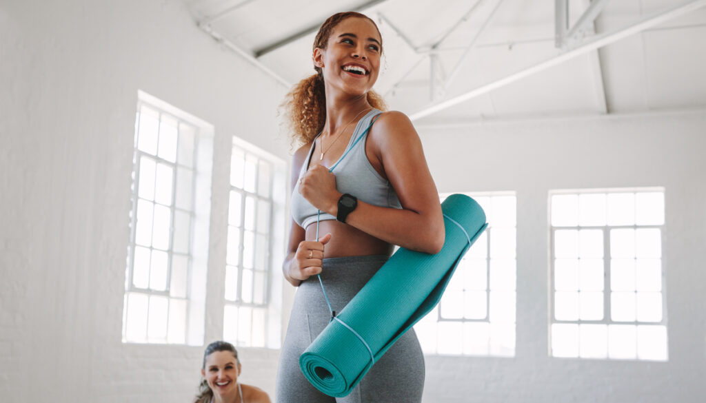 woman leaving yoga class with yoga mat smiling