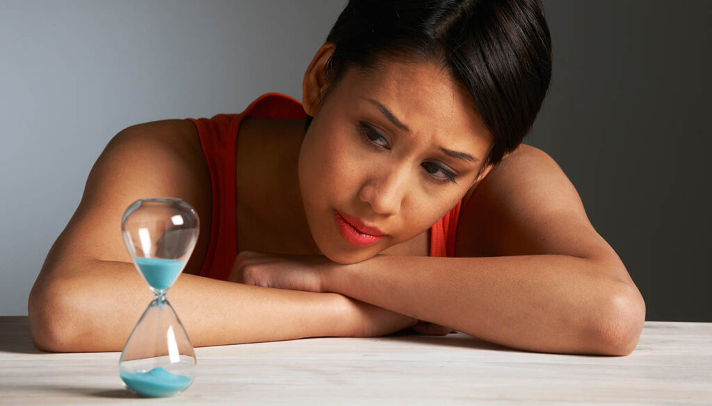 Sad Young Woman Looking At Hourglass