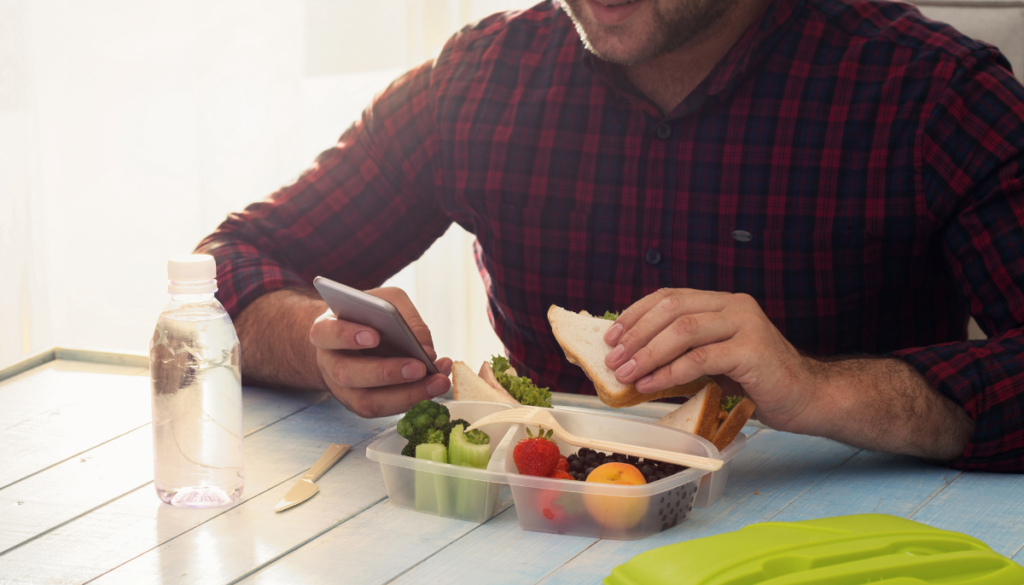 Man checking phone while eating lunch from reusable container