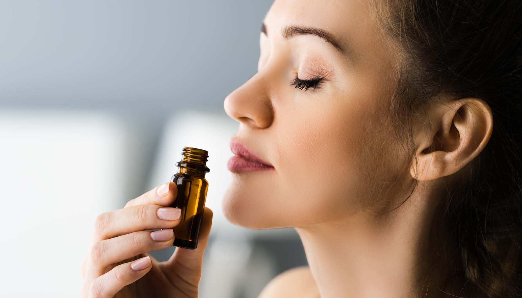 woman deeply inhaling scent of aromatherapy oil with her eyes closed