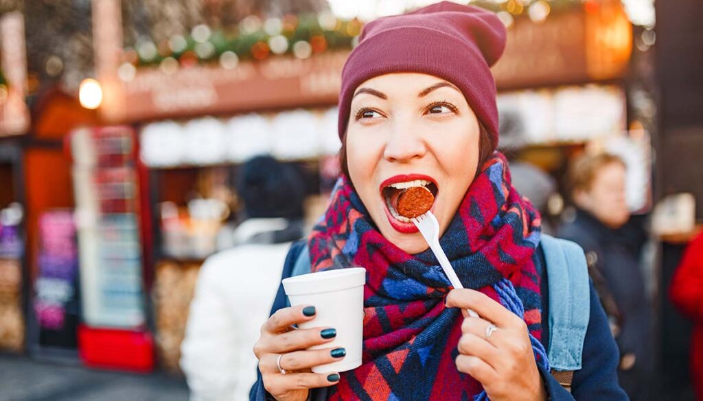 young woman traveler snacks a sausage with a hot drink on the street of a European city in the winter