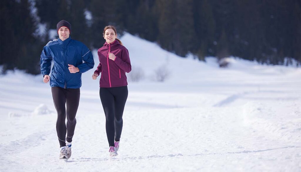 healthy young couple jogging outside in forest on snowy winter day. 