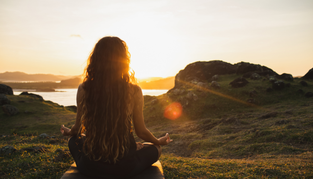 Woman sitting in lotus yoga pose outside at sunset