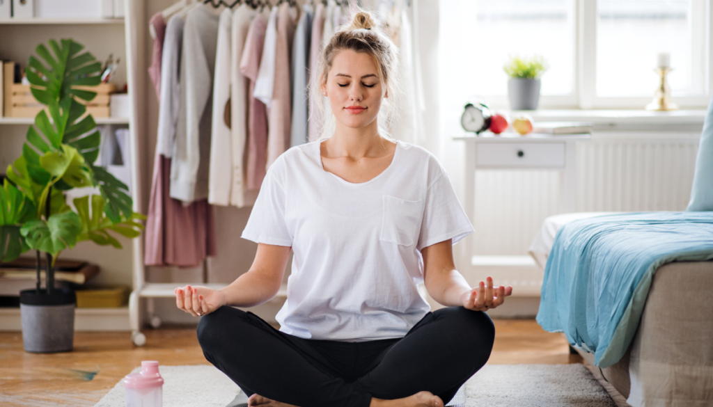 Woman sitting in lotus yoga pose in bedroom