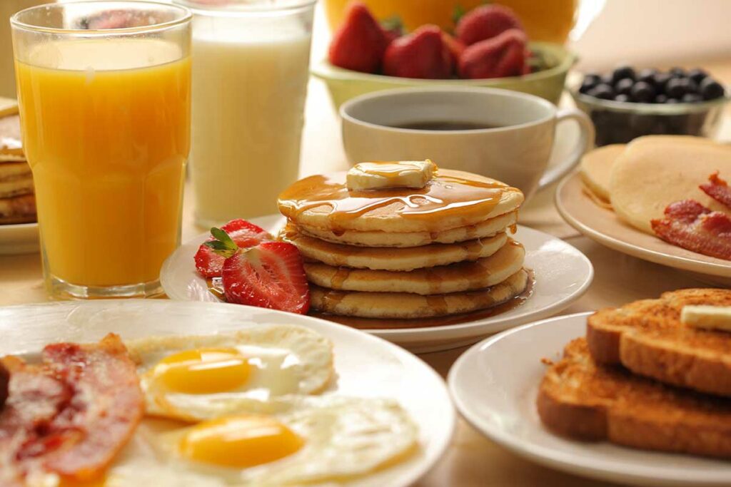 lots of breakfast foods: juice, milk, coffee, pancakes, eggs, toast, bacon, fruit
