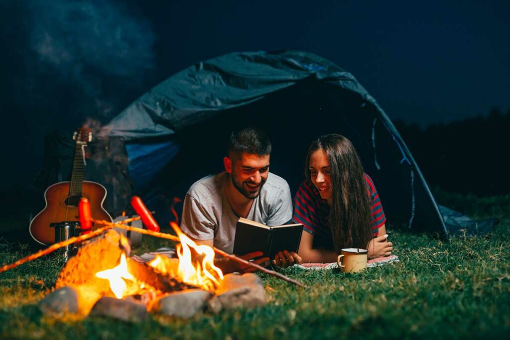 couple reading a book at night in a camping tent with fire