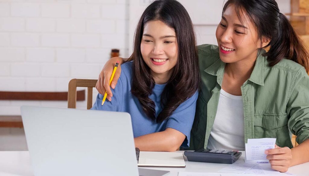 Asian lesbain couple together calculate home budget with paper bill and laptop in new house at table in kitchen