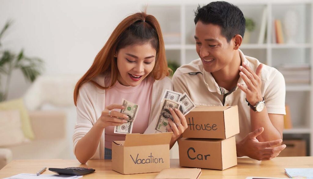 Portrait of young Asian couple putting money to piggy banks, saving for house, car and vacation