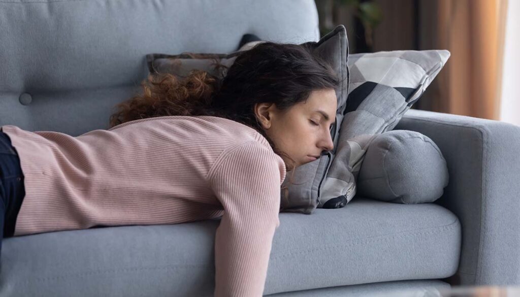 exhausted woman sleeping on her stomach on a couch