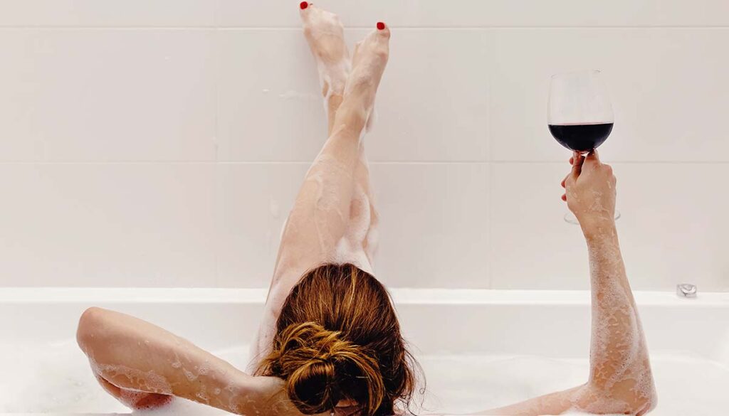 woman in bubble bath with her feet on the wall and a glass of wine in hand