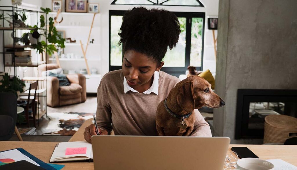 woman making notes at desk with small dog in her lap