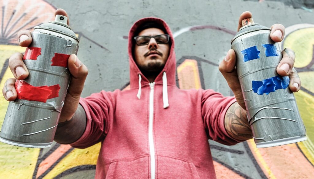 a man in a hoodie holding two spray paint cans