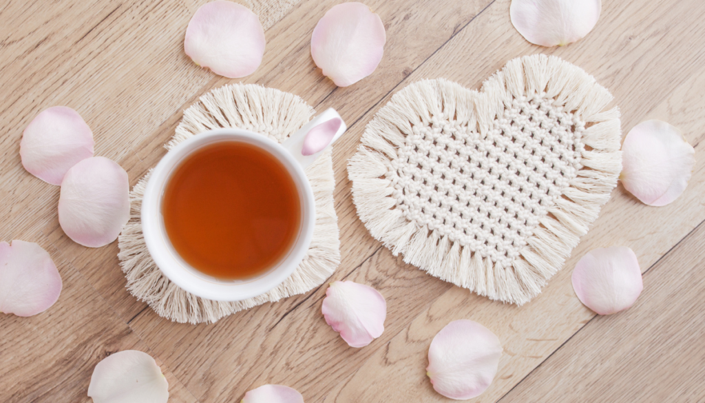 Cup of tea next to heart shaped rope coaster with flower petals