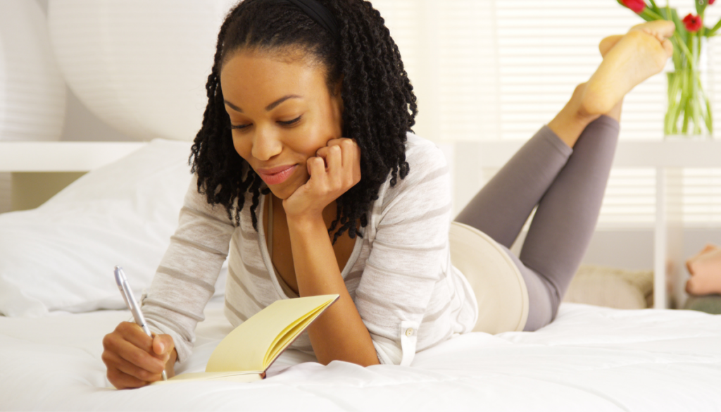 Woman laying on bed writing in notebook