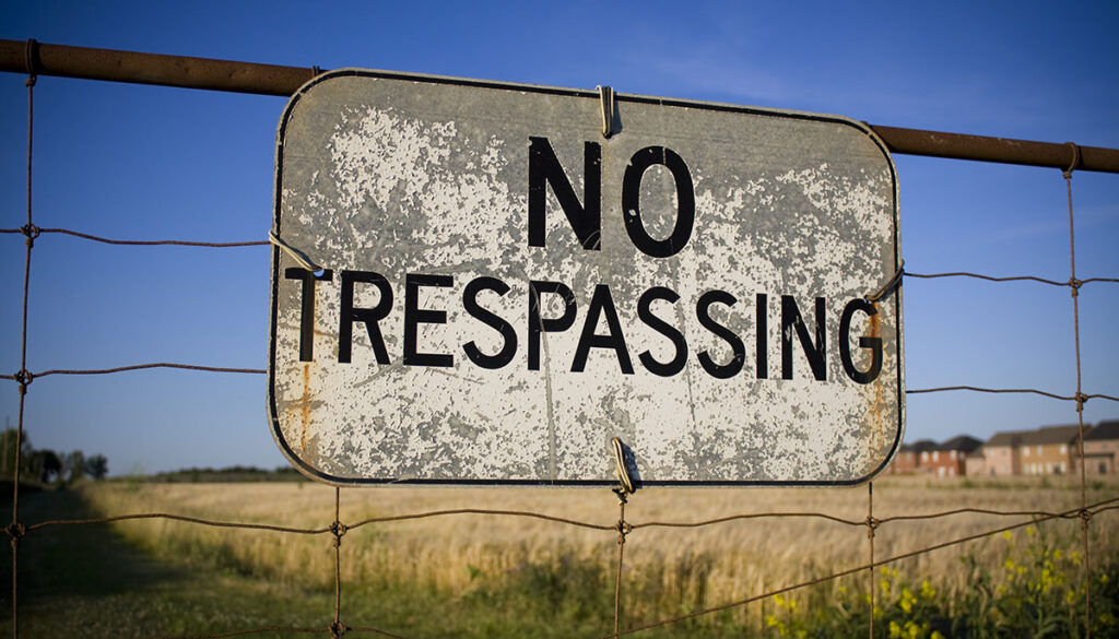 No trespassing sign against backdrop of farmland and houses