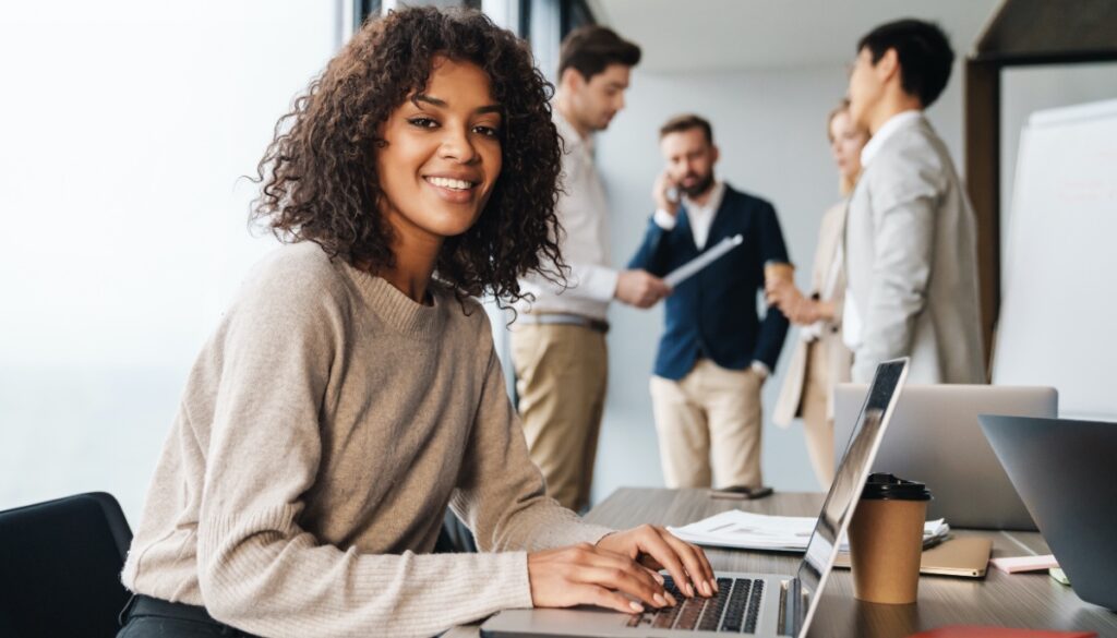 Woman typing at desk with colleagues in the background