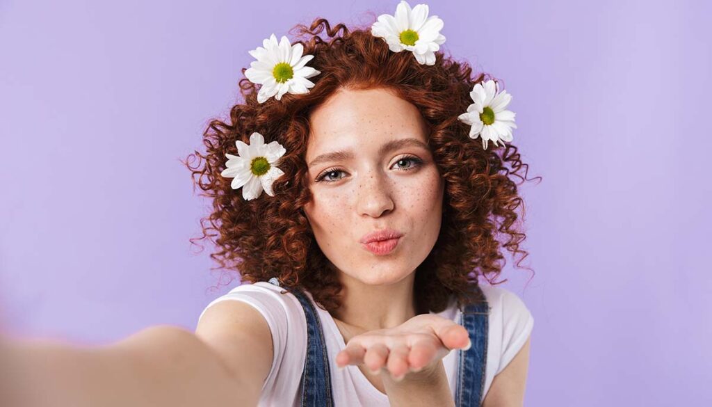 red headed young woman blowing kiss with daisies in her hair