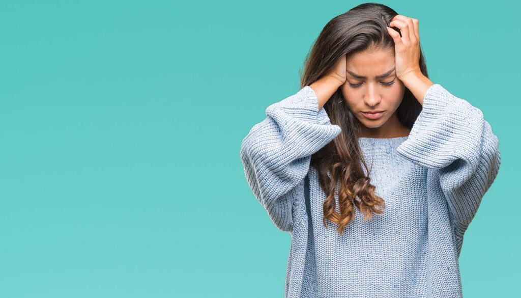 woman holding her head distressed wearing blue sweater