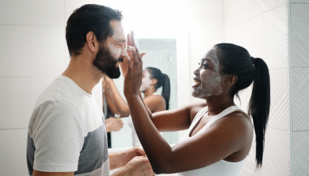 Woman with a face mask helping male partner rub in face mask
