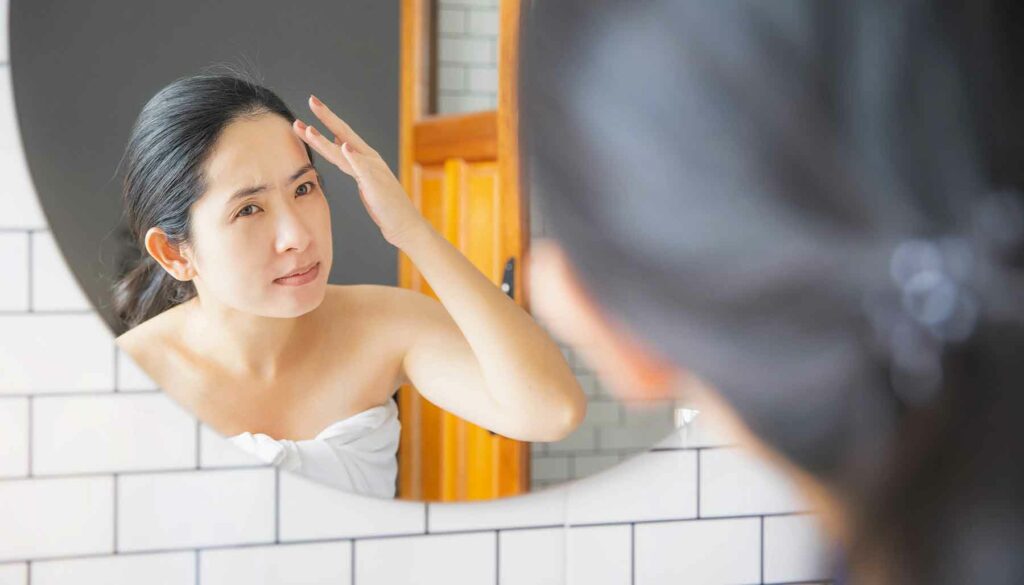 woman looking at her face in bathroom mirror