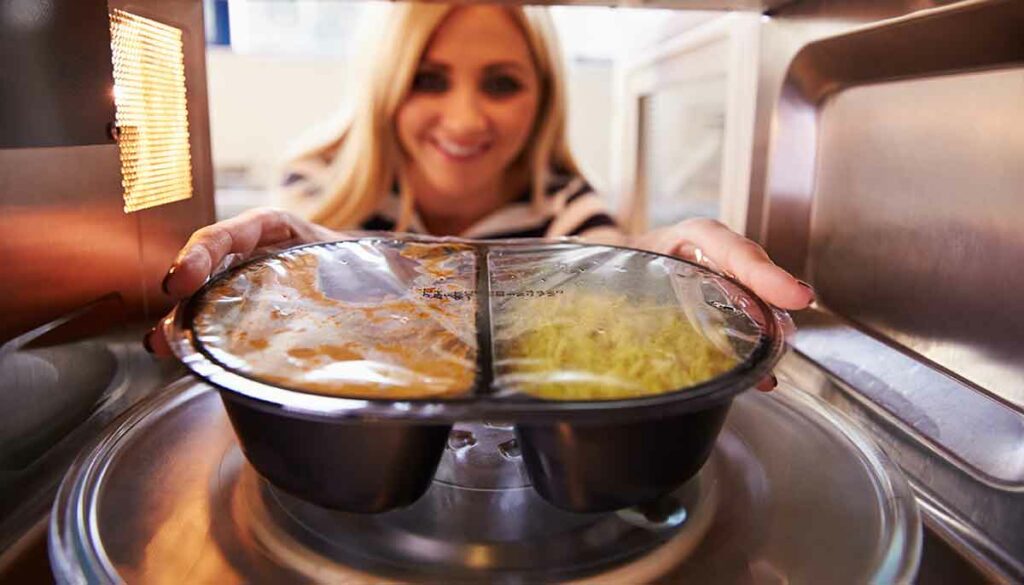 woman cooking a frozen dinner in a microwave