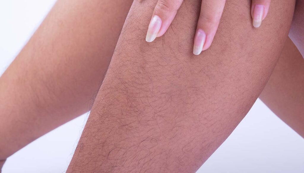 woman with long fingernails touching leg hairs